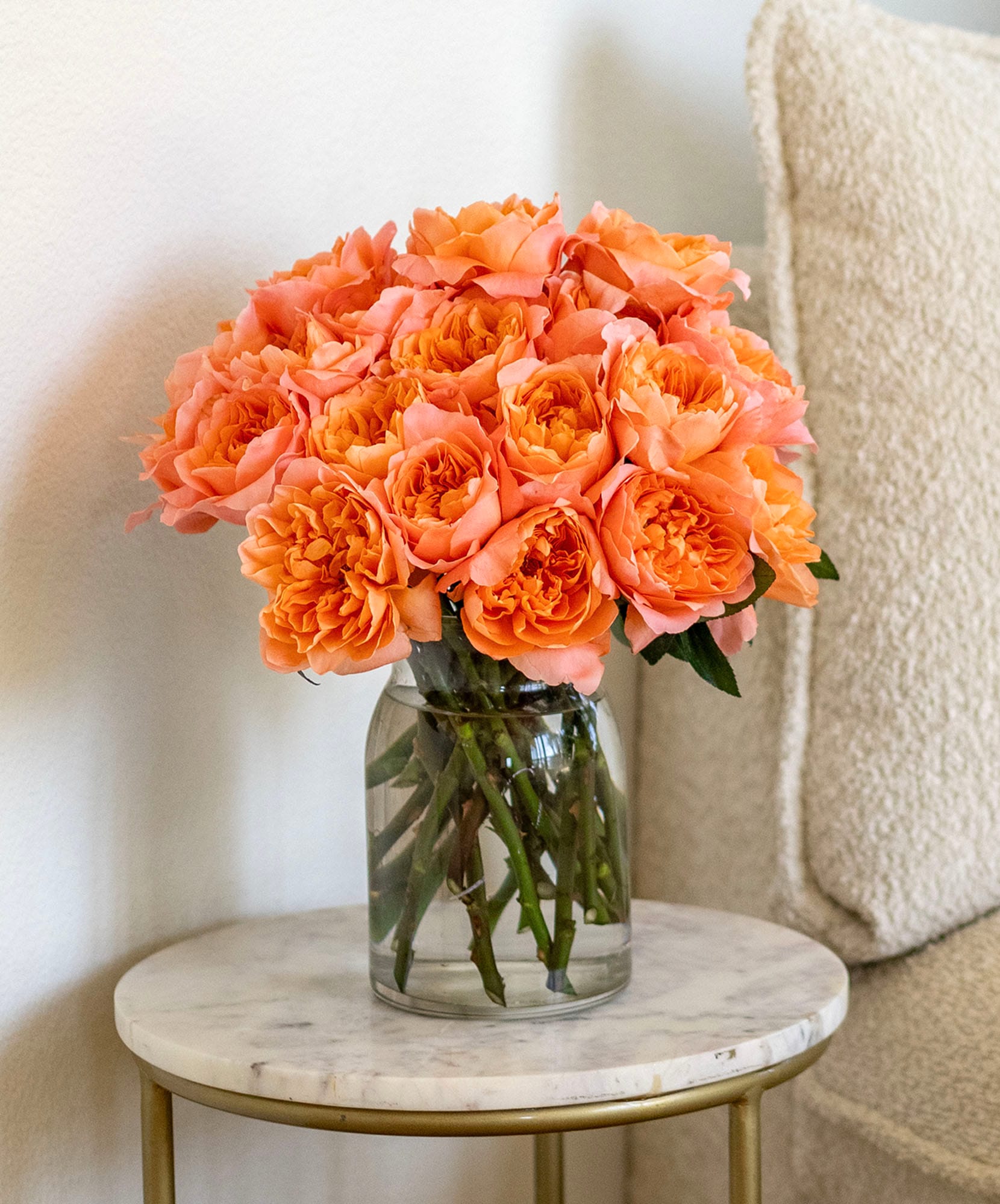 Vibrant peach roses elegantly arranged in a glass vase on a stylish table.